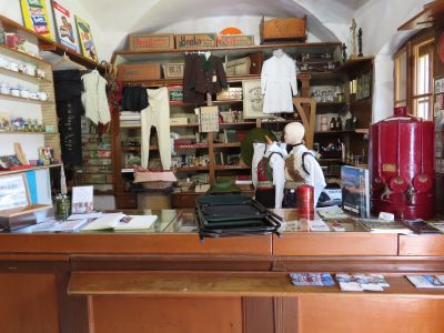 Das Verkaufspult mit Geschirr, drei Emailletafeln, Kartons, zwei Schaufensterpuppen in Gailtaler Tracht und dem roten Petroleumspender im Greißlermuseum Thörl-Maglern